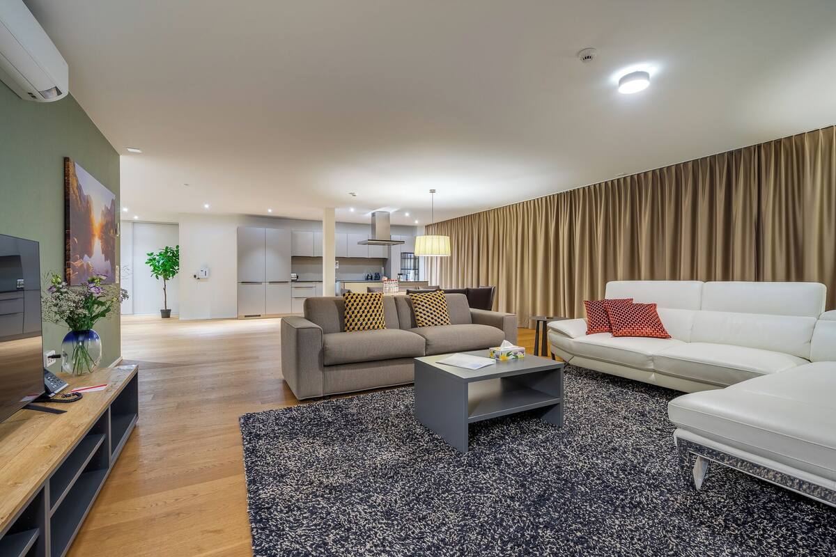 Un salon moderne avec un canapé gris, un canapé blanc, une table basse et un téléviseur posé sur un meuble en bois.