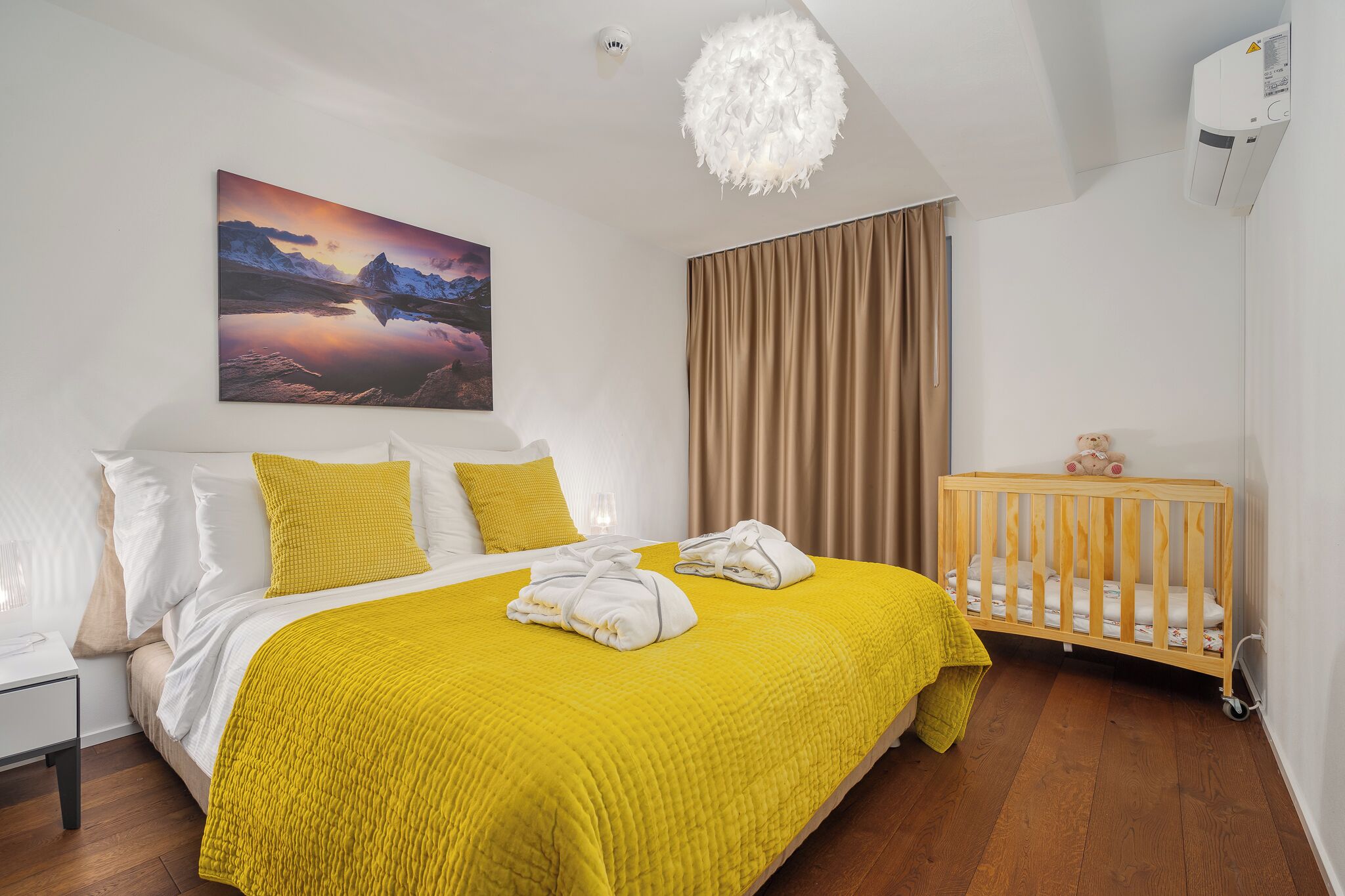 A hotel room with a bed, a crib, a painting, and a ceiling light.