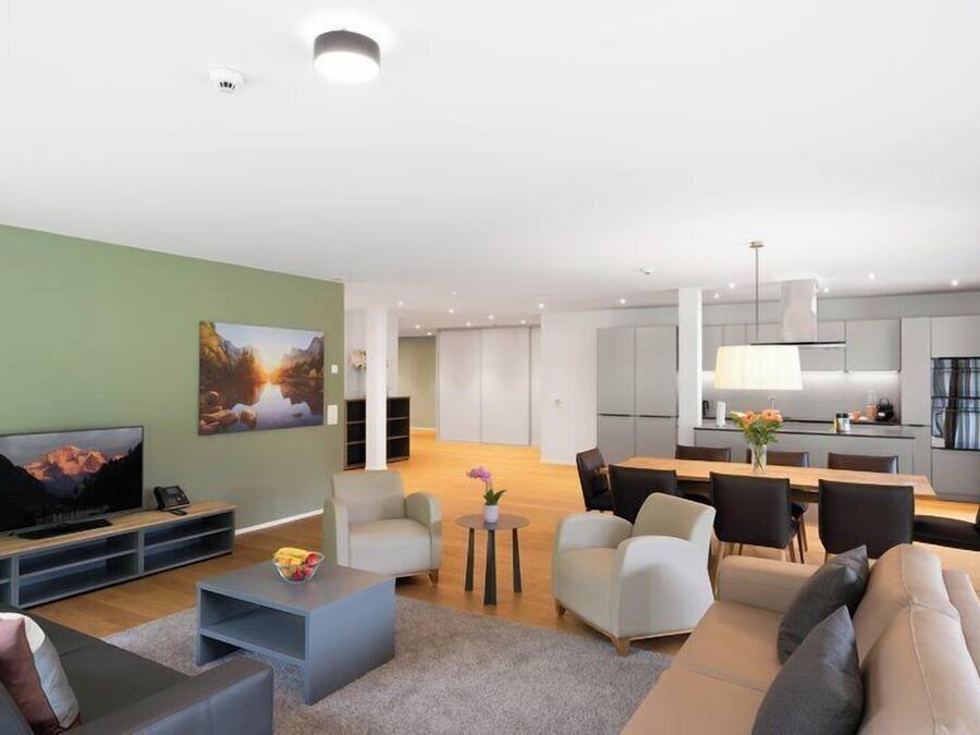 Una sala de estar moderna con televisor de pantalla plana, sofás, una mesa de centro y un comedor con sillas.