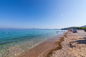 Ein Strand mit klarem Wasser, Kieselsteinen und Menschen.