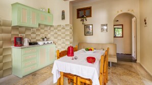 A dining area with a table set for four, a green kitchen with a coffee maker, and a small window with a view. - Ipsos Marias Apartments By Konnect (Corfu)