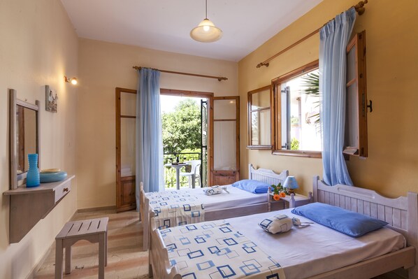 A room with two beds, a small table, a bench, and a window with curtains.