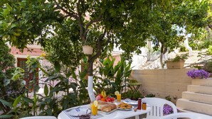 An outdoor dining area with a table set for two, surrounded by greenery and a staircase. - Ipsos Marias Apartments By Konnect (Corfu)