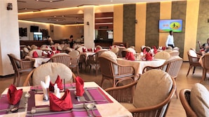 A restaurant with wicker chairs and tables set with red napkins and silverware. - Verona Hotel & Conference Center (Ruiru)