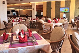 A restaurant with wicker chairs and tables set with red napkins and silverware.
