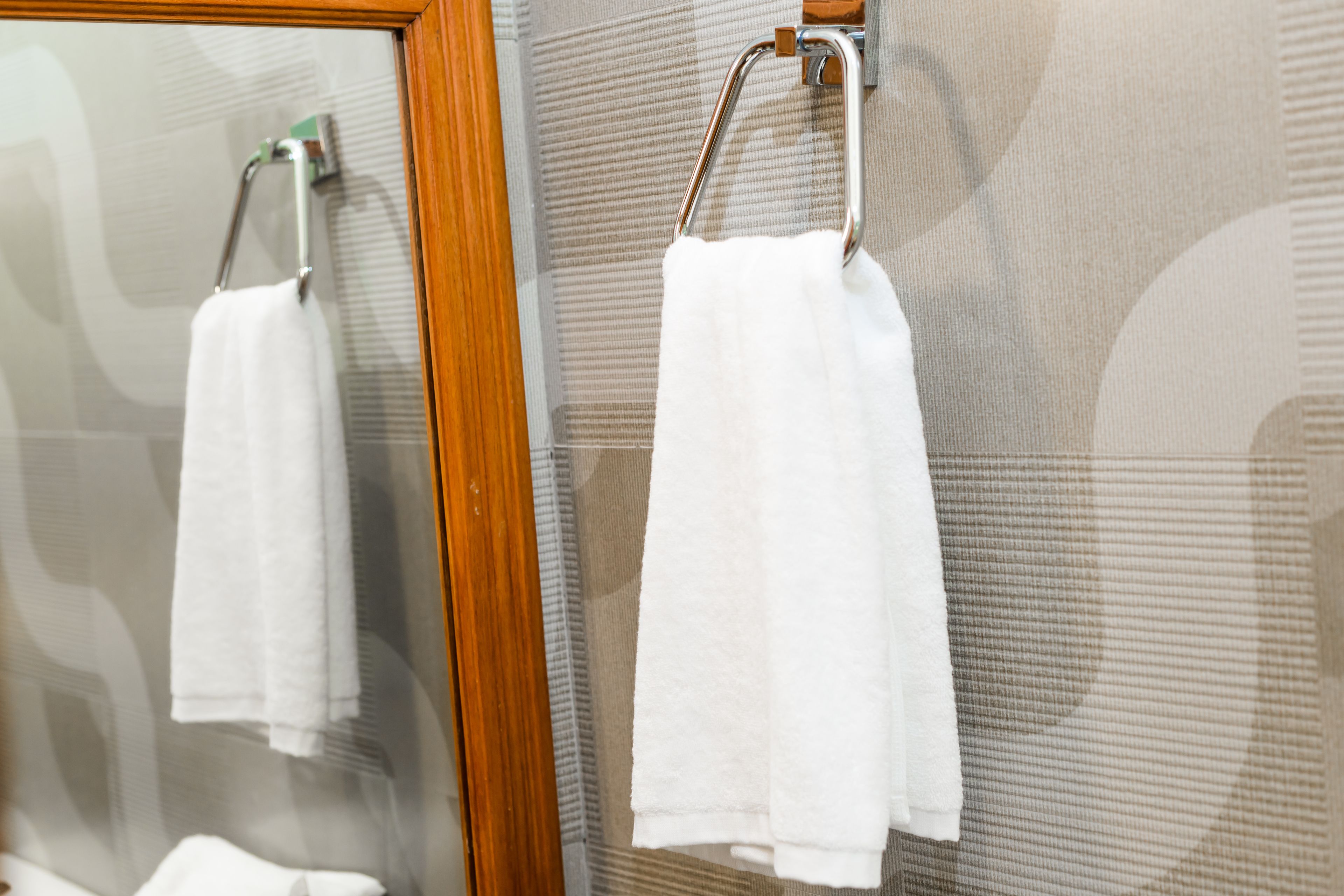 A bathroom with two white towels hanging on towel racks, a wooden frame around the mirror, and a textured wall.