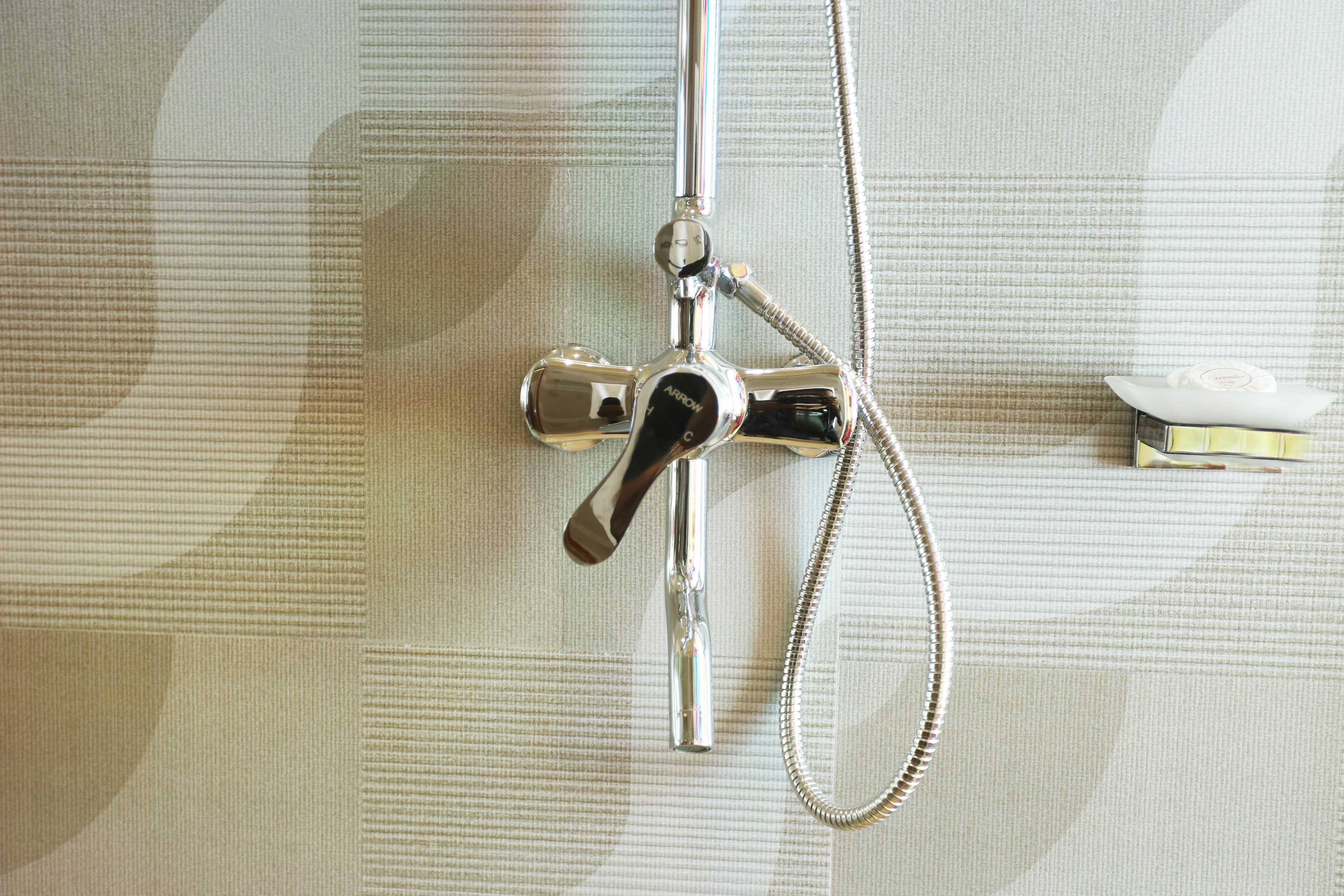Un cabezal de ducha con un accesorio de mano y una manguera flexible, instalado en una pared con textura.