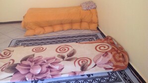 Una habitación pequeña con una cama cubierta por un edredón estampado de flores y una manta naranja lisa.