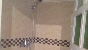 Ducha con borde de azulejos a cuadros y puerta de vidrio.