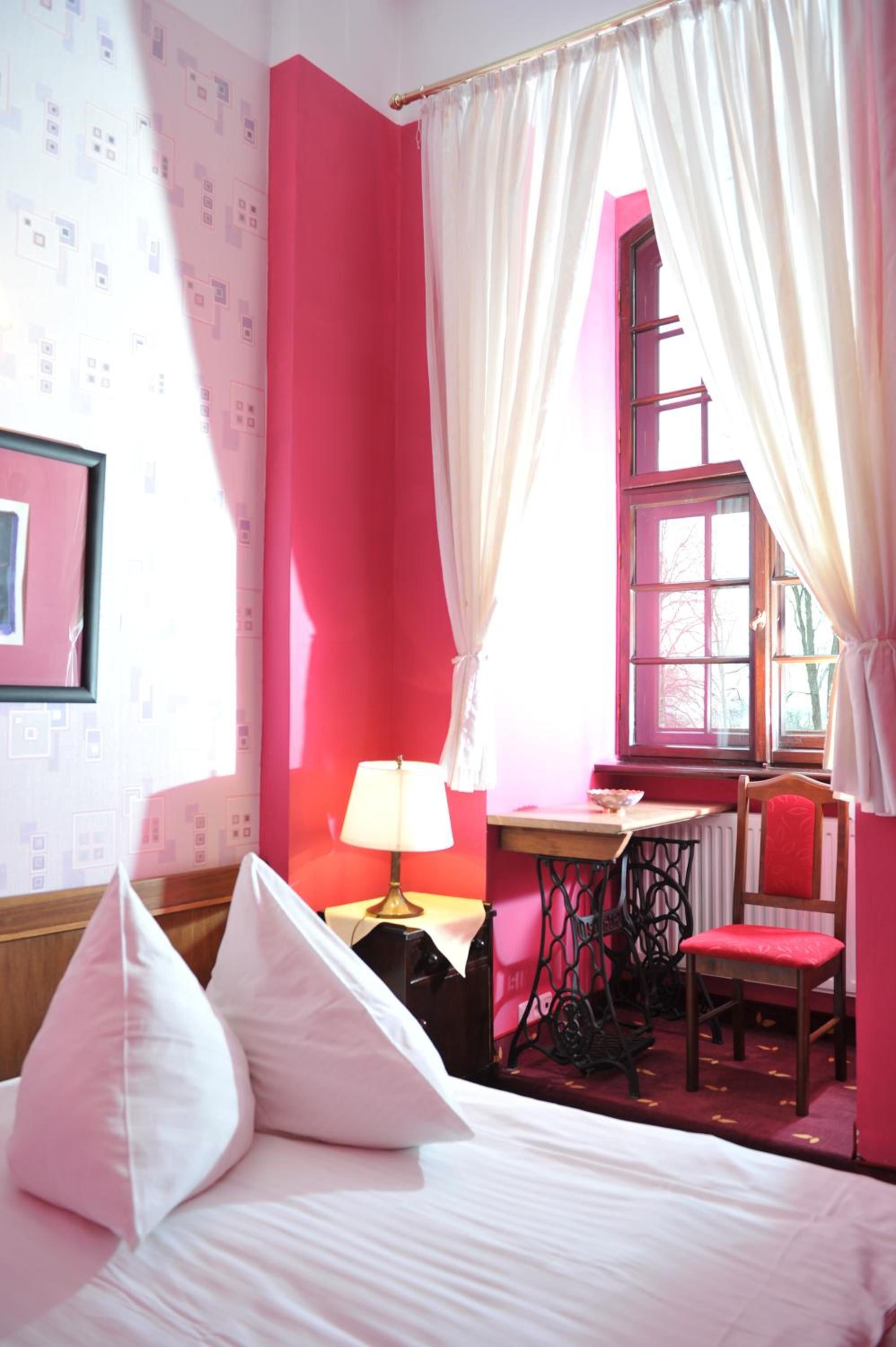 A room with a bed, a desk, a chair, and a window with curtains.