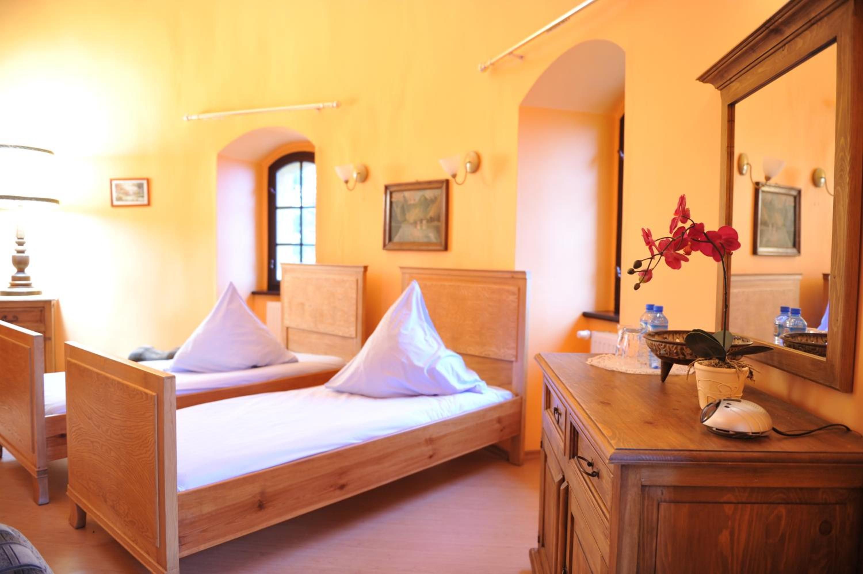 A room with two wooden beds, a dresser, a mirror, and a vase with flowers.