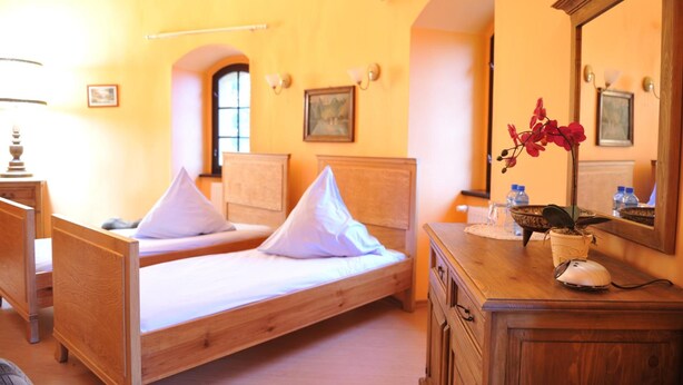 A room with two wooden beds, a dresser, a mirror, and a vase with flowers. - Zamek Dobra (Dobroszyce)