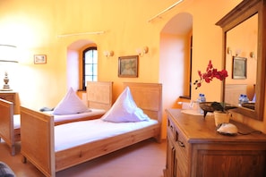 Una habitación con dos camas de madera, un aparador, un espejo y un florero con flores.