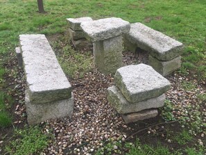 A stone bench with a flat top and a backrest, surrounded by pebbles and grass. - Zamek Dobra (Dobroszyce)