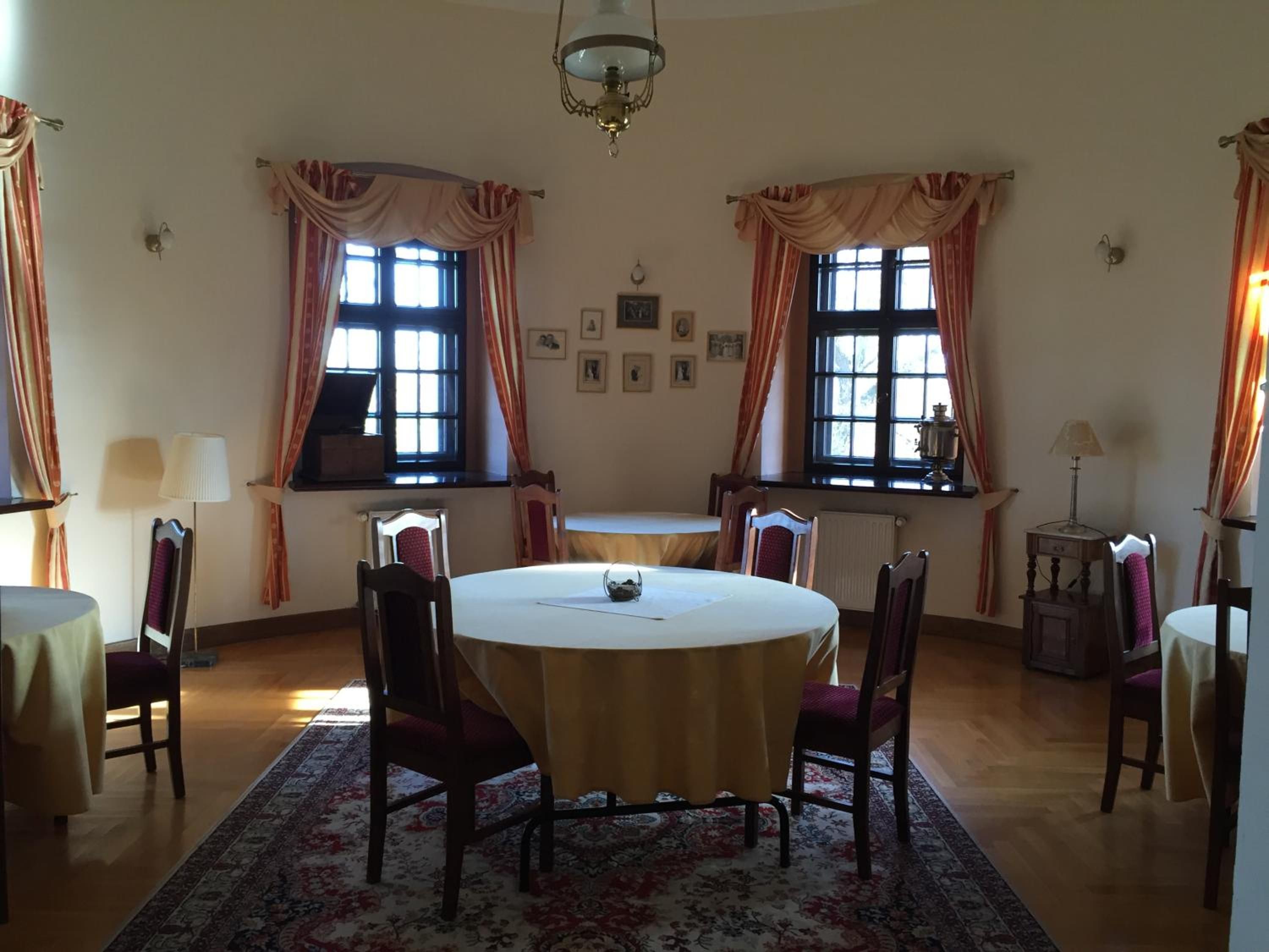 A dining room with a round table, chairs, a chandelier, and windows with curtains.