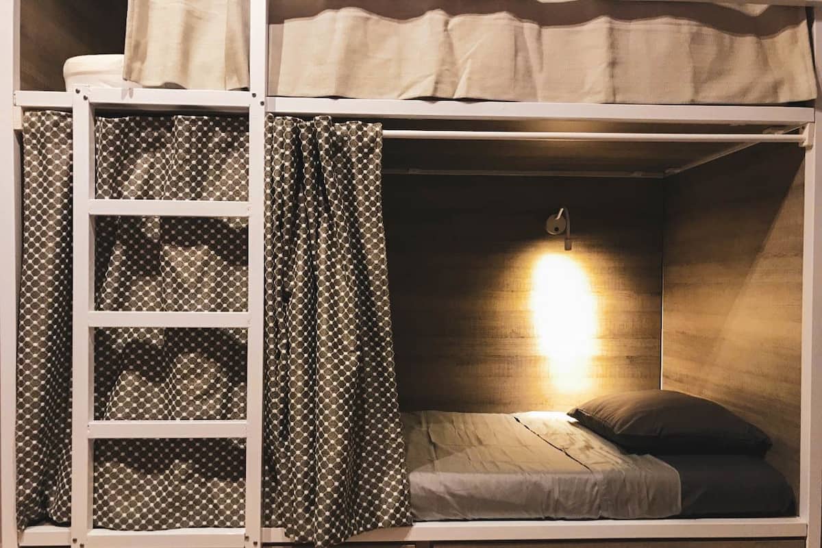 Una cama litera con escalera, una lámpara de noche y una cortina.