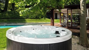 Ein Whirlpool mit Holzverkleidung, umgeben von einer Terrasse und einer Glaseinfriedung mit Trainingsgeräten.