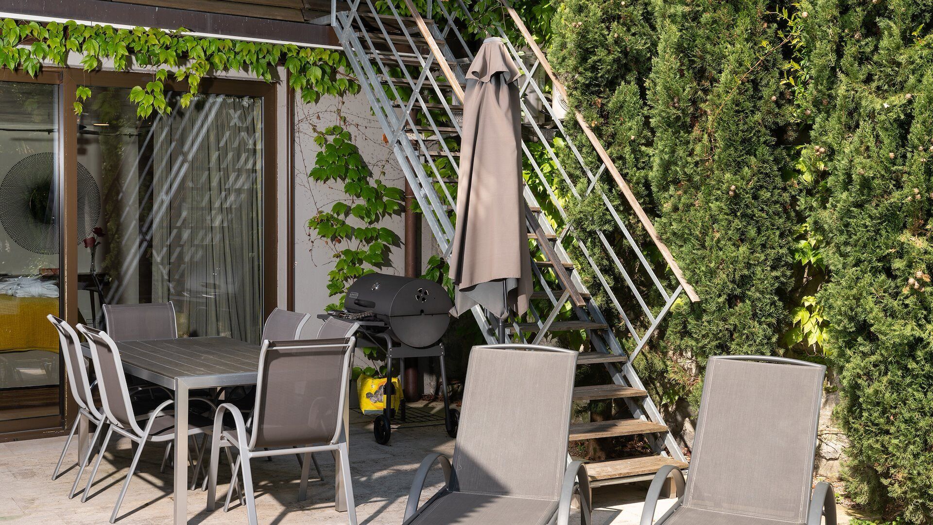 Un patio al aire libre con una mesa y sillas, una parrilla y un área cubierta con una escalera.