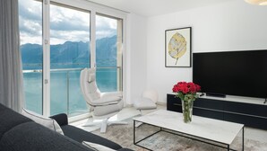 Een moderne woonkamer met een groot raam, een flatscreen televisie, een witte bank, een bijzettafeltje en een vaas rode rozen.