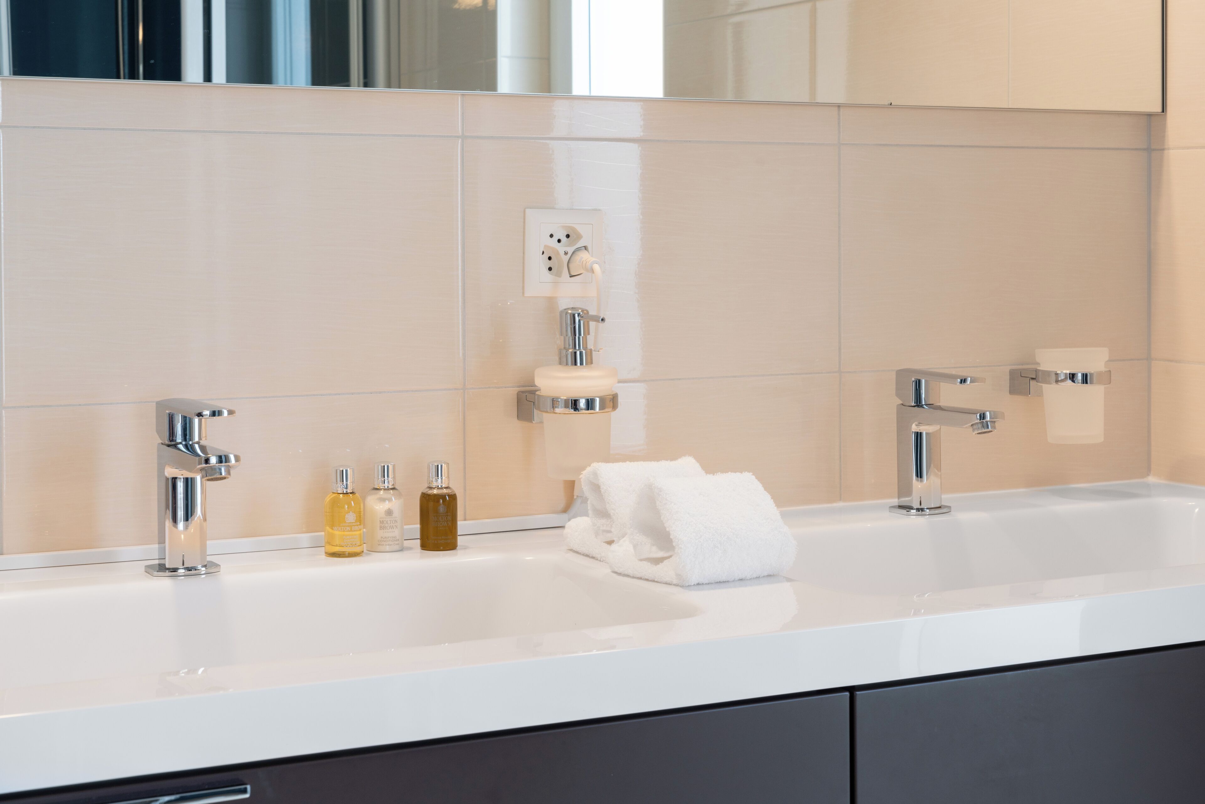 A modern bathroom with a white sink, two faucets, a mirror, and a towel.