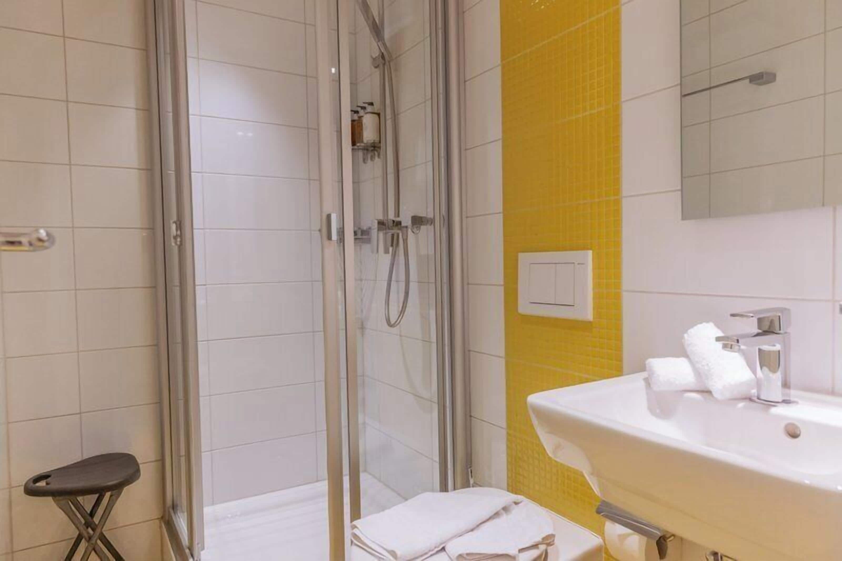 A bathroom with a glass-enclosed shower, a white sink with a mirror, and a yellow accent wall.