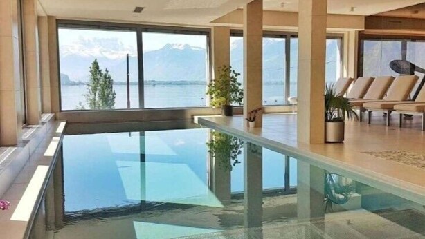 Een modern interieur met een zwembad met glazen bodem, grote ramen en uitzicht op bergen.