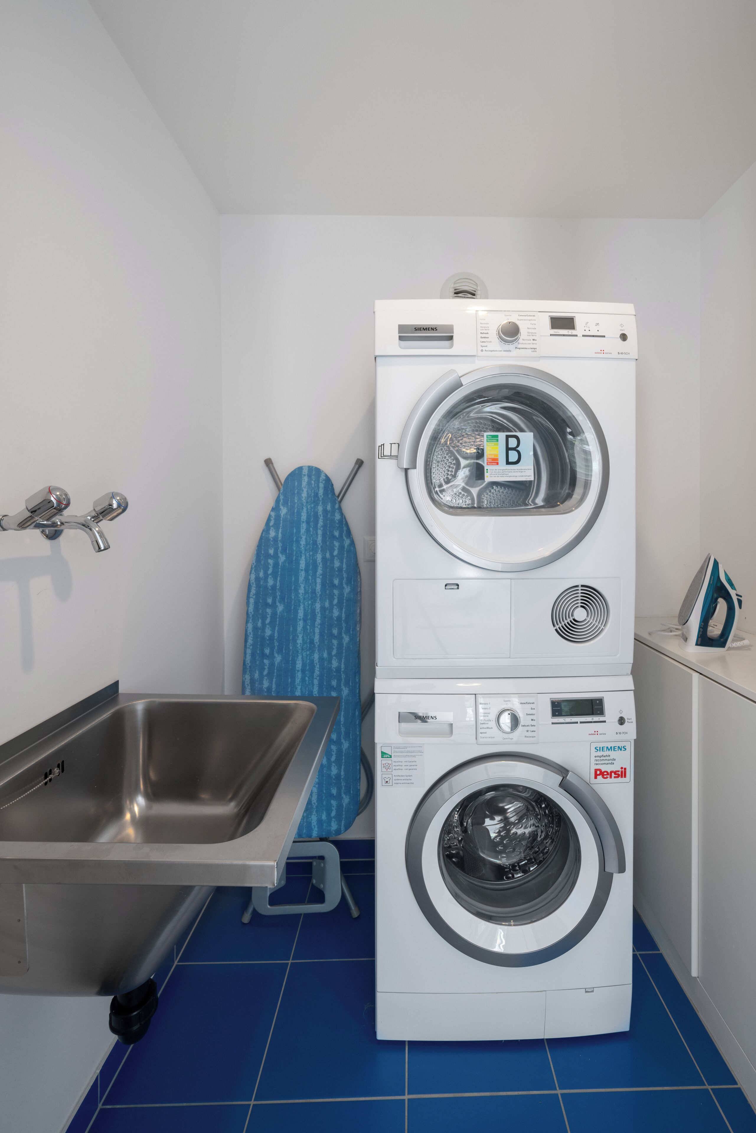 A laundry area with stacked washers and dryers, a sink, and an ironing board.