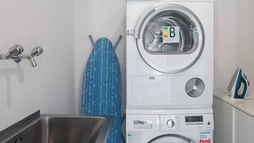 A laundry area with stacked washers and dryers, a sink, and an ironing board.