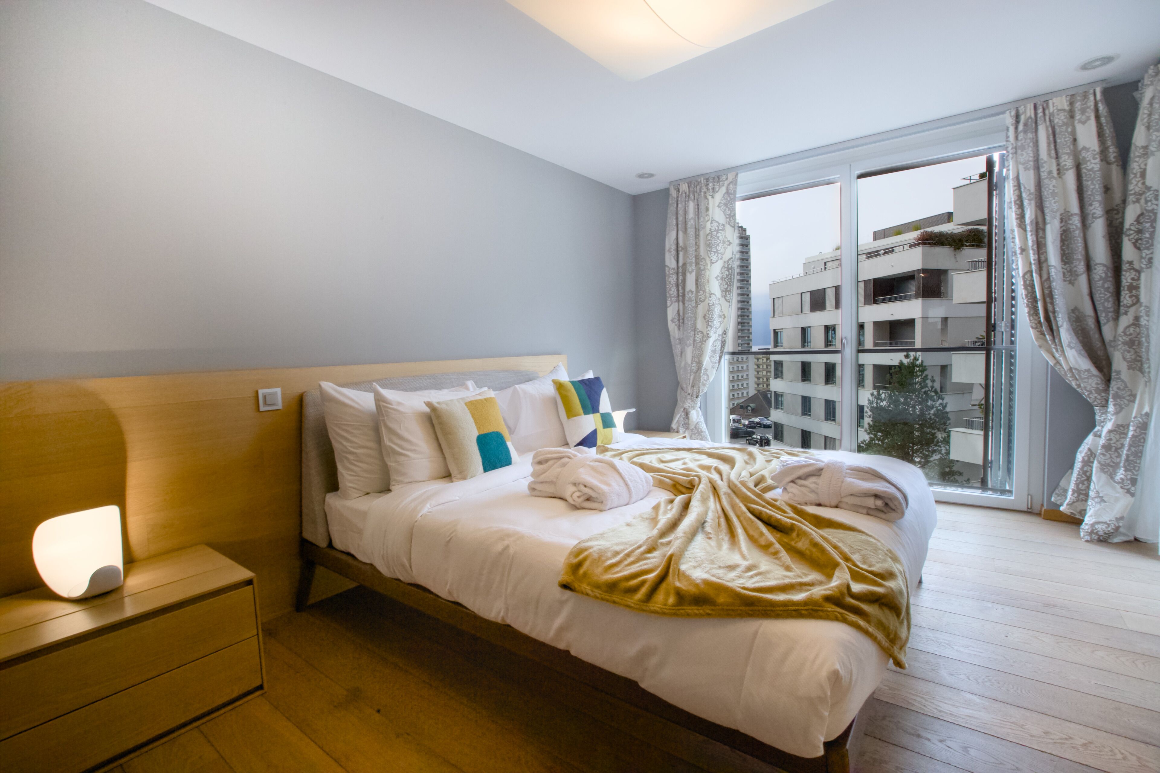 Un dormitorio con cama, mesita de noche y ventana con cortinas.