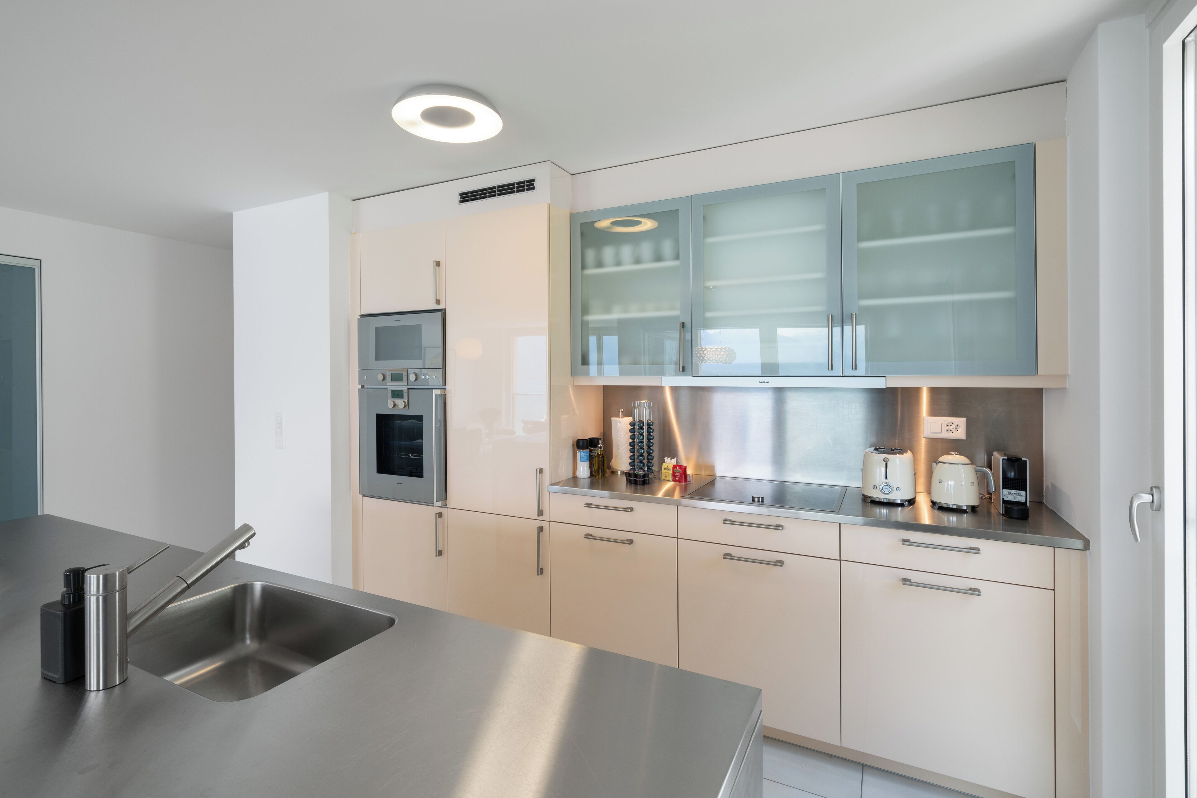 Une cuisine moderne dotée d’appareils électroménagers en acier inoxydable, de meubles de rangement de couleur claire et d  ’un four encastré.