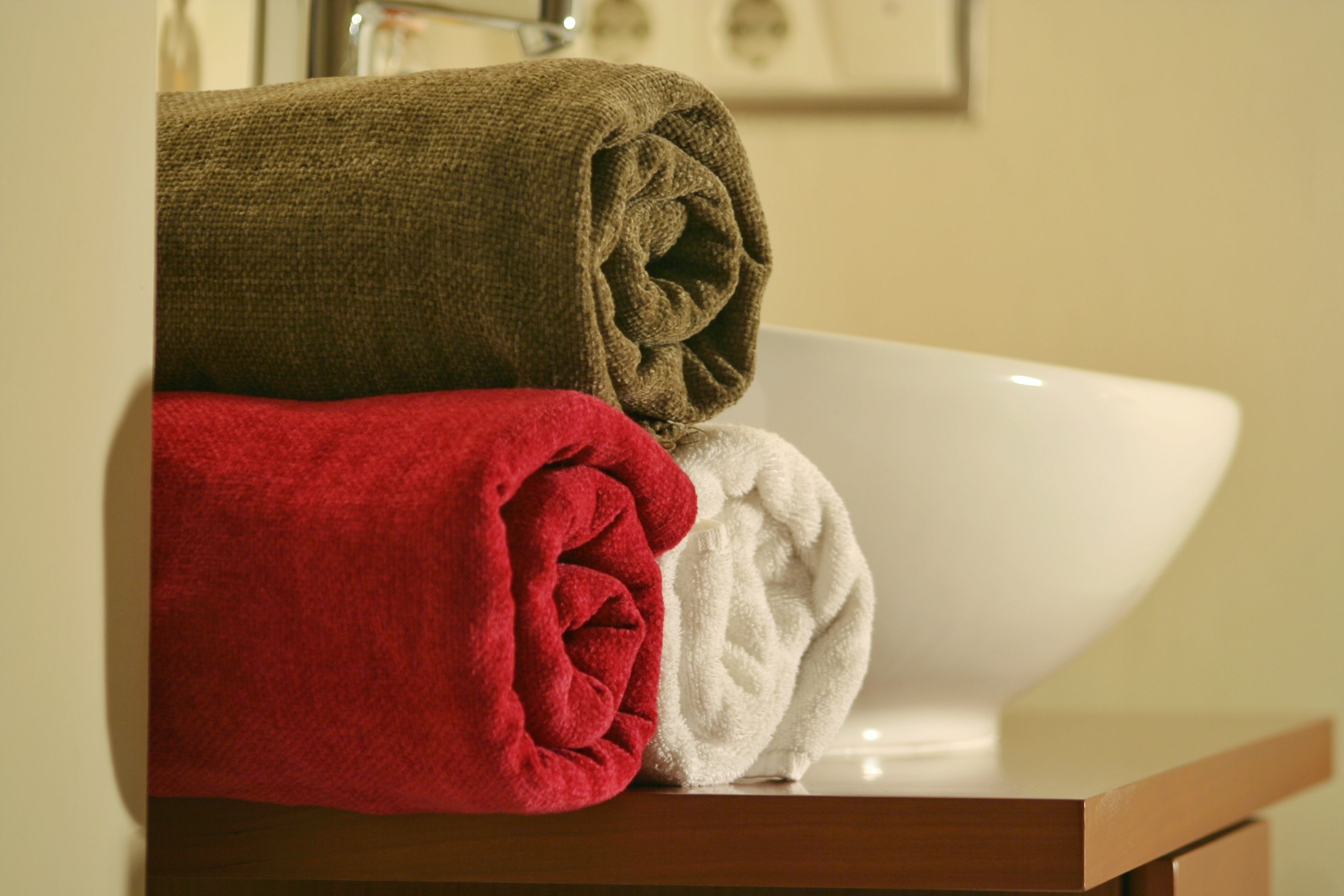A bathroom with a white sink and three rolled towels in brown, red, and white.