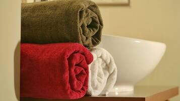 A bathroom with a white sink and three rolled towels in brown, red, and white.