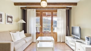 Una sala de estar con sofá, mesa de centro, televisor y ventana con cortinas.
