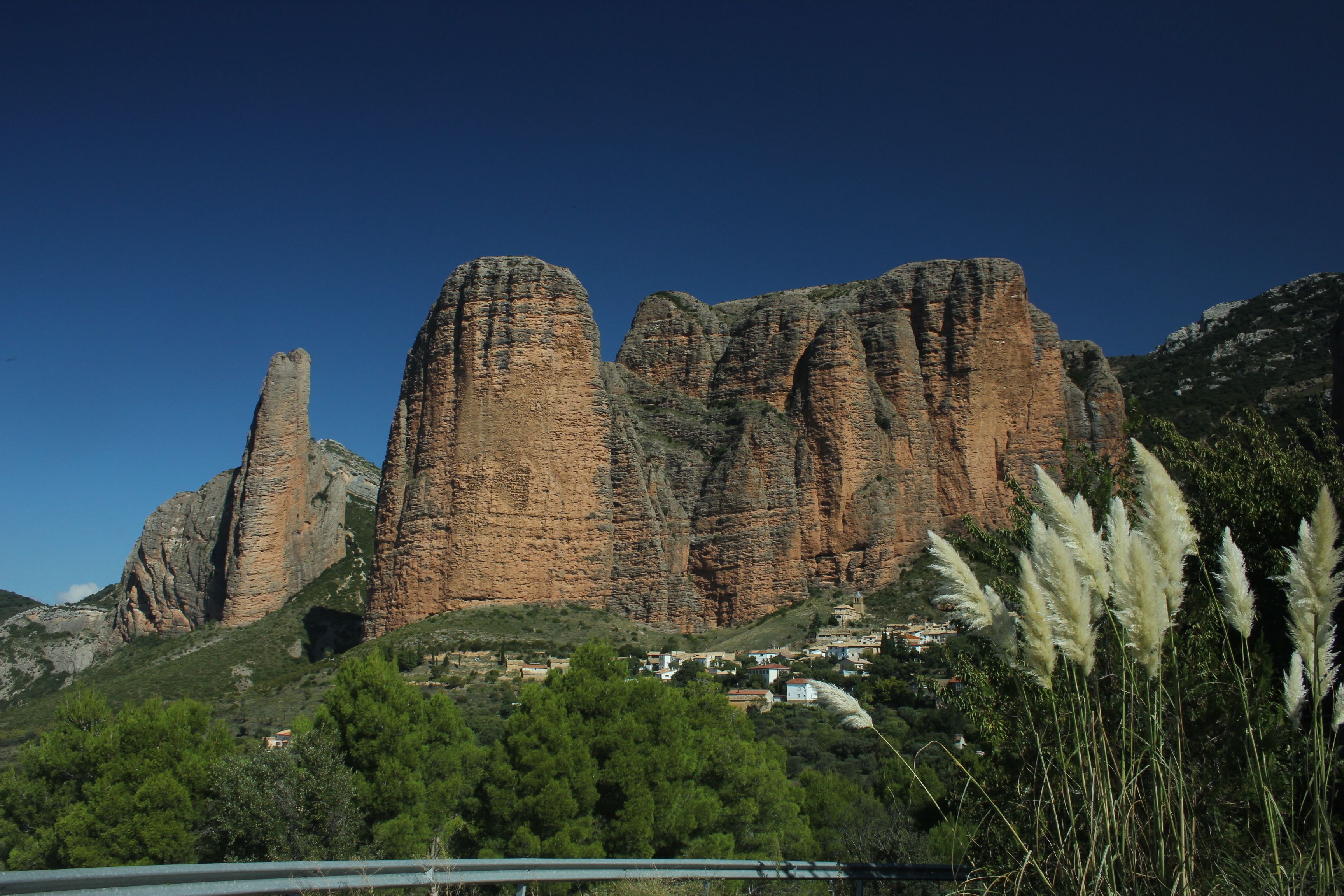 A mountainous landscape with prominent rock formations and a small settlement at the base.