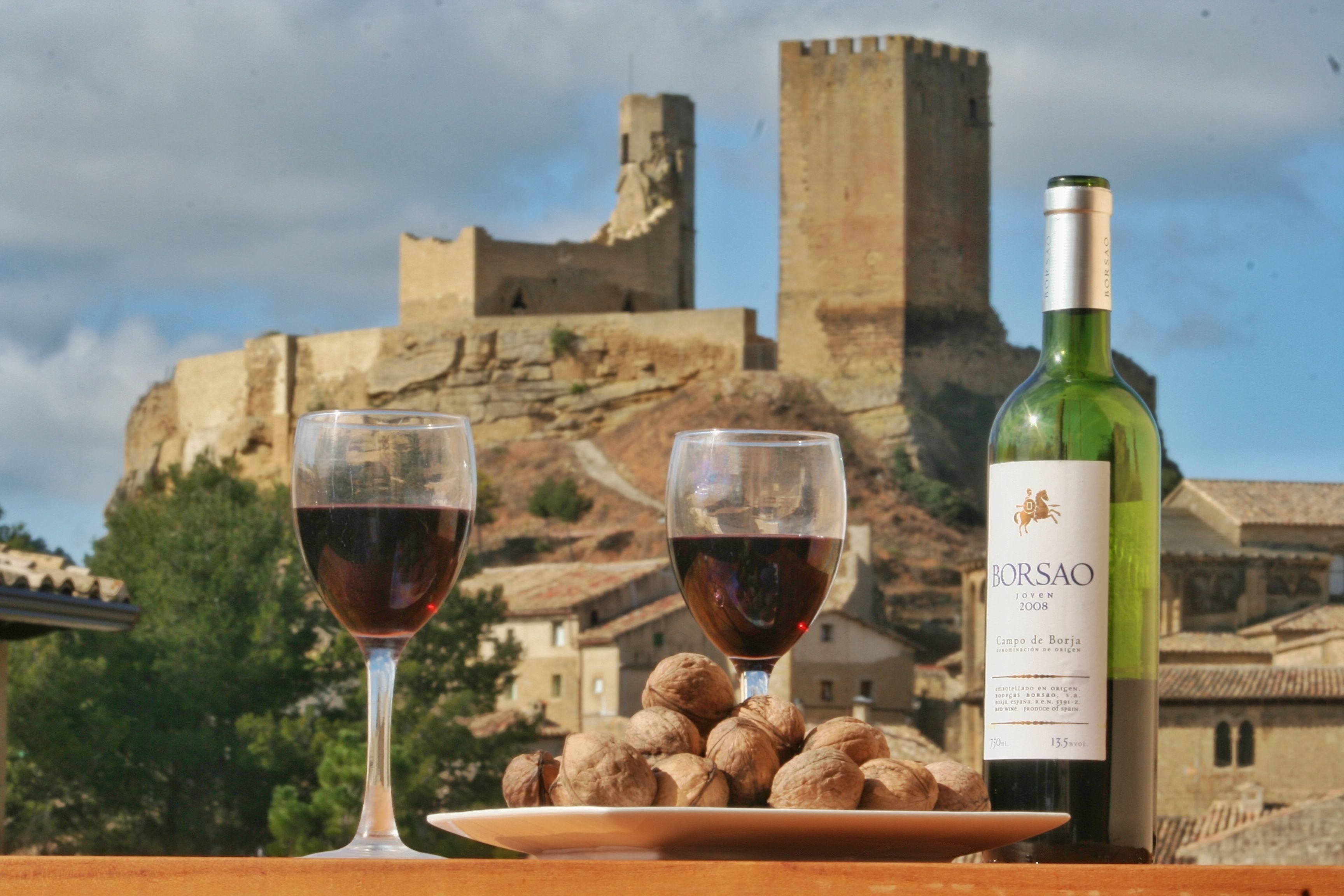 Duas taças de vinho e uma garrafa de vinho Borsao Joven 2008, com um prato de nozes e uma vista de um castelo histórico ao fundo.