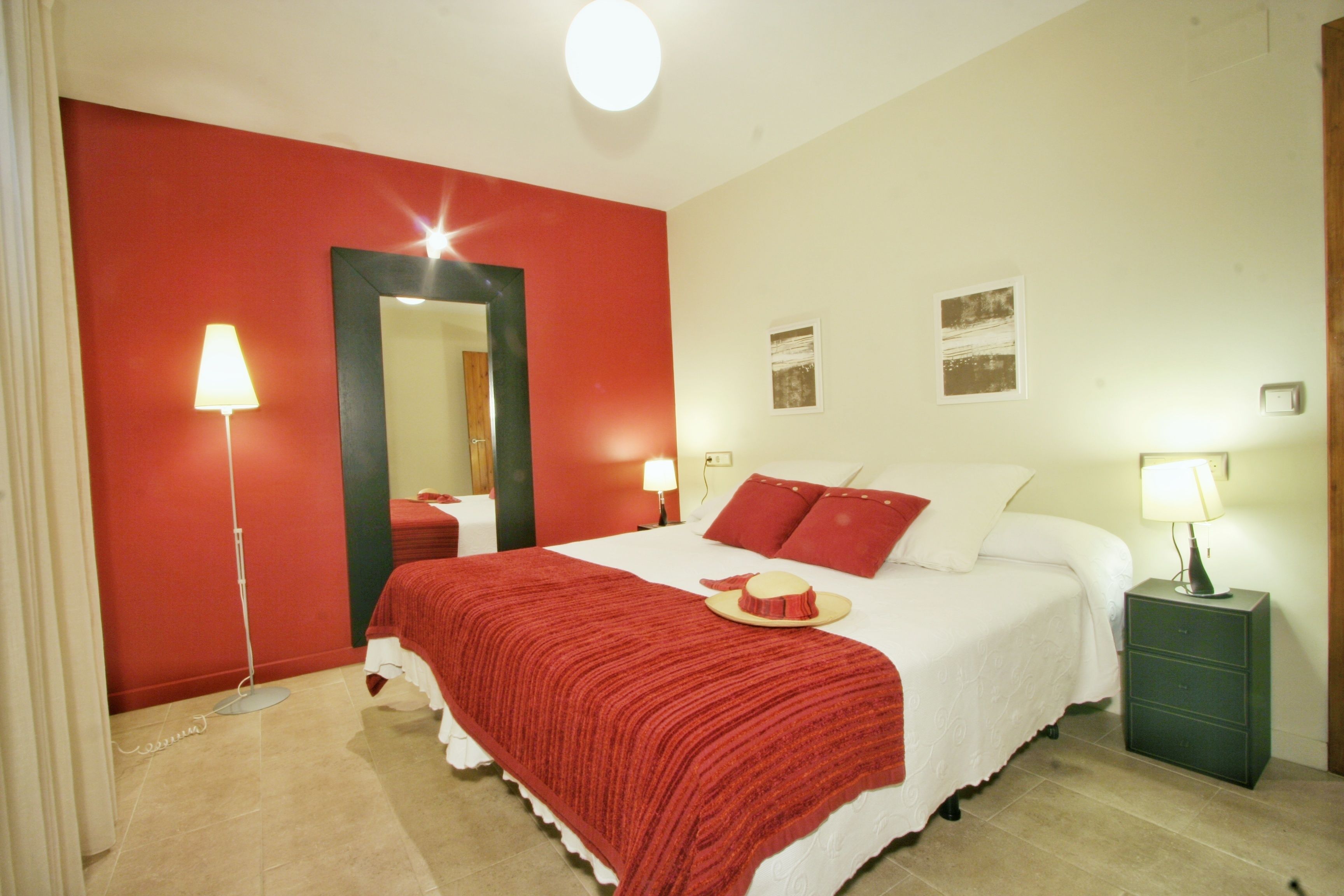 Habitación de hotel con una pared de acento roja, una cama grande con ropa de cama blanca, dos mesitas de noche con lámparas y un espejo sobre la cama.