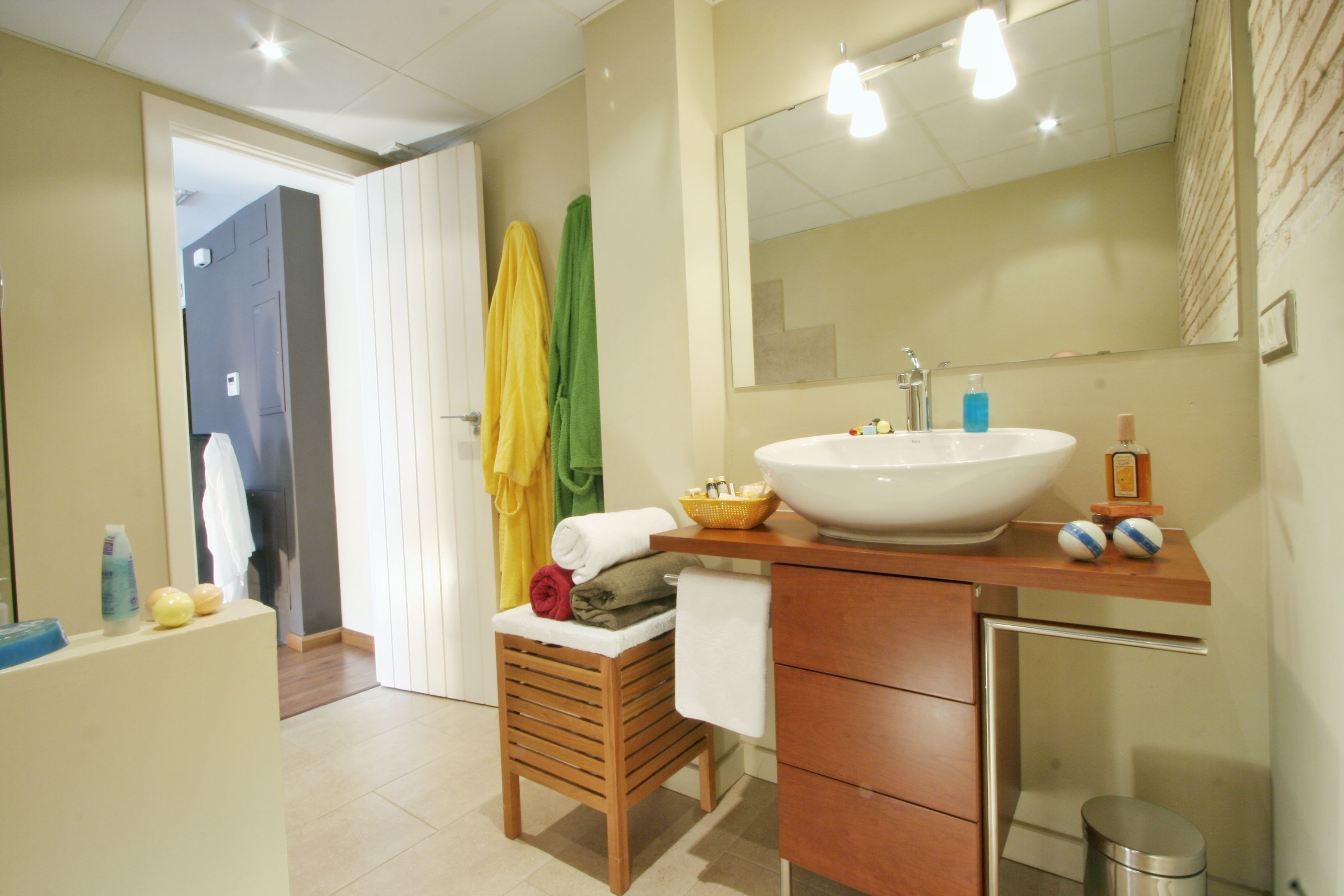 A bathroom with a wooden vanity, a large mirror, a white sink, and a small stool with towels.