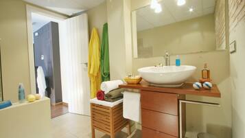 A bathroom with a wooden vanity, a large mirror, a white sink, and a small stool with towels.