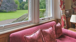 A room with a view of a green lawn and trees through a window. - Tillmouth Park Country House Hotel (Cornhill on Tweed)