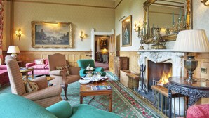 A traditional room with a fireplace, green and pink upholstered furniture, and classic decor including wall sconces and framed artwork. - Tillmouth Park Country House Hotel (Cornhill on Tweed)