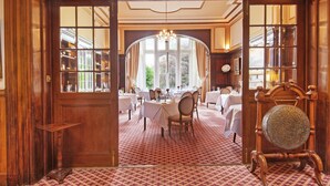 A formal dining room with multiple tables set for service, a large arched window, and a classic wooden interior. - Tillmouth Park Country House Hotel (Cornhill on Tweed)