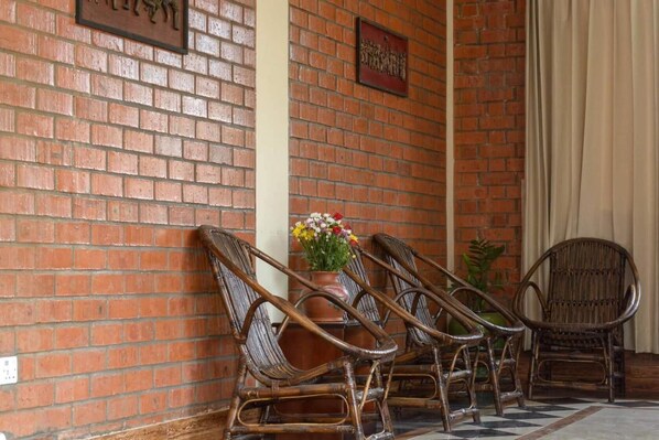 Un mur de briques, deux chaises en osier et une table agrémentée d’un arrangement floral.