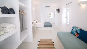 A modern, well-lit room with a bed, a sofa, and a wardrobe. - Apanomeria Residence (Santorini)