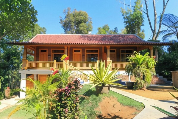 Una casa de madera con techo de tejas rojas, un balcón y un jardín con diversas plantas.