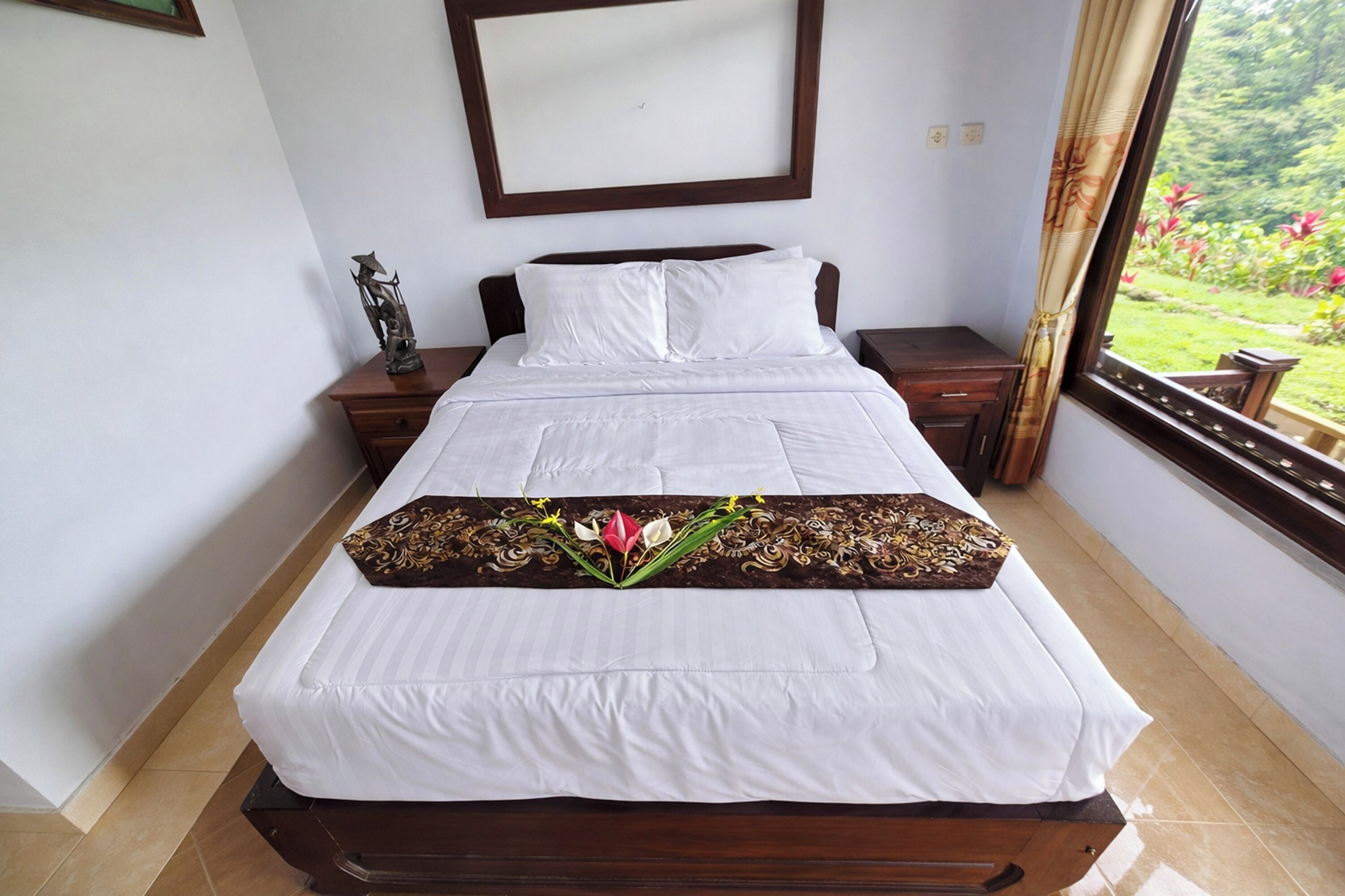 A neatly made bed with white linens, a decorative pillow, and a floral arrangement on the bedspread.