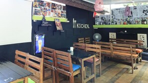 A cozy cafe with wooden furniture, a black wall with the name 'KOCHEN', and a variety of drinks on the counter. - Kubu Turah Homestay (Kedonganan)