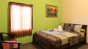 A bedroom with a bed, a chair, a window with curtains, and a painting on the wall. - Kubu Turah Homestay (Kedonganan)