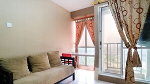 Una sala de estar con un sofá, una mesita y un balcón con cortinas.