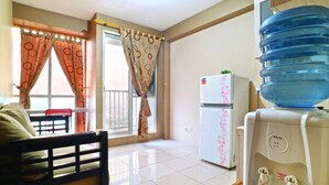Una habitación con cama, dispensador de agua, refrigerador y ventana con cortinas.