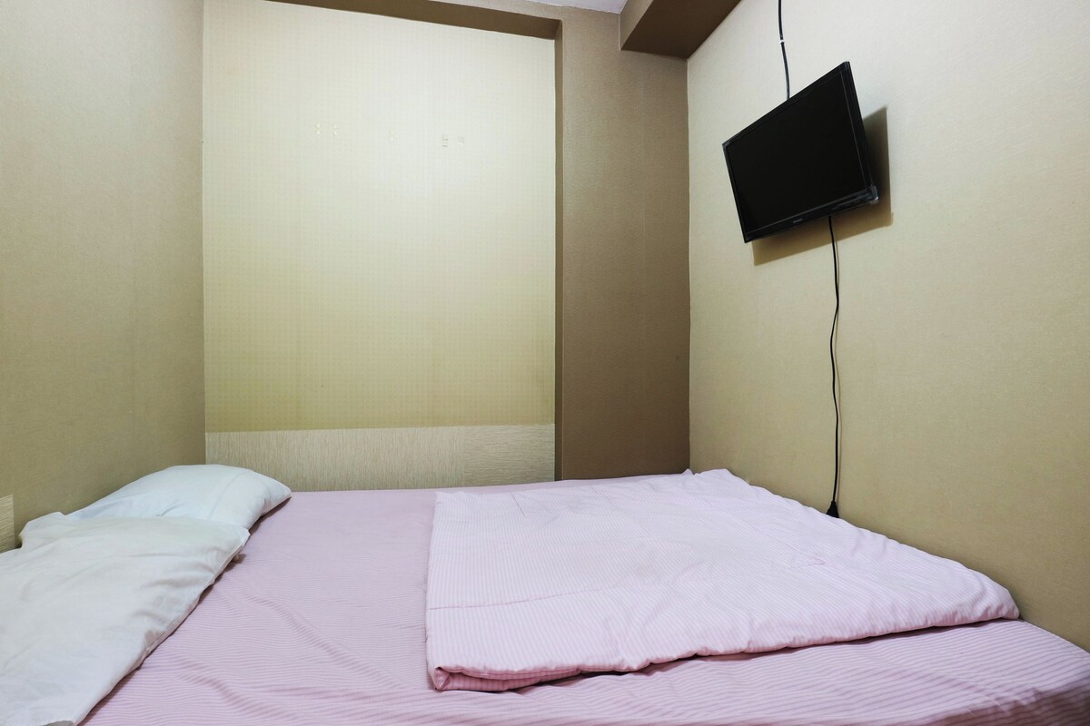 Una habitación con una cama, un televisor montado en la pared y un ventanal.